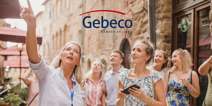Eine Reisegruppe folgt einer Stadtführerin, die in einer historischen Altstadt auf ein Gebäude zeigt. Die Teilnehmer lächeln und schauen interessiert nach oben. Im oberen Bereich ist das Logo von „Gebeco“ eingeblendet.