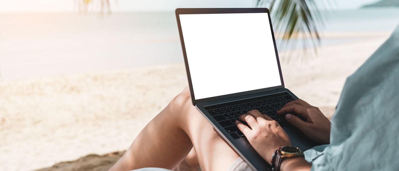 Person mit Laptop arbeitet am Strand