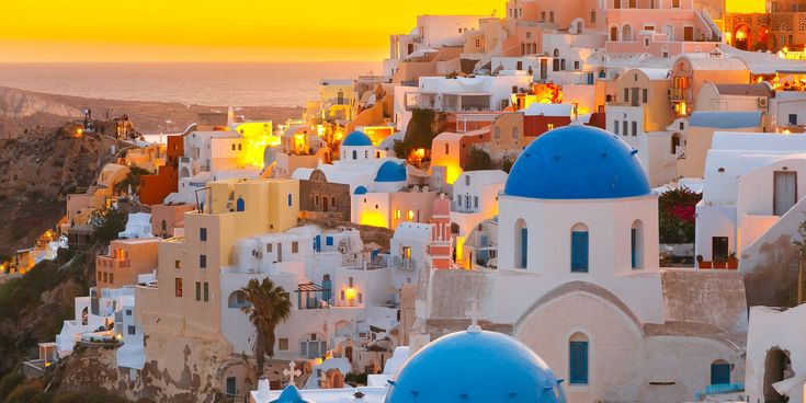 Blick auf die weiß-blauen Häuser von Oia auf Santorini bei Sonnenuntergang mit goldenem Licht über der Ägäis.