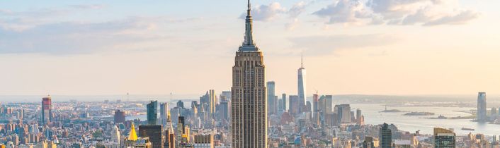 Blick auf die Skyline von Manhattan mit dem Empire State Building und Hudson River im warmen Abendlicht.