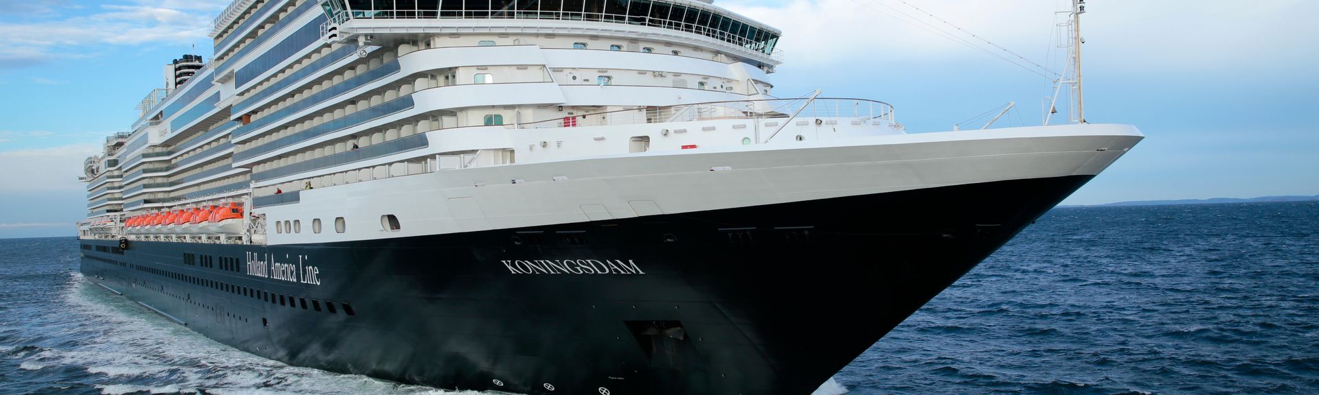 Ein großes, modernes Kreuzfahrtschiff fährt durch das offene Meer und schneidet mit seinem Bug dynamisch durch die Wellen.