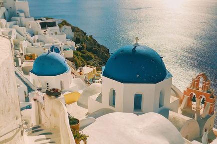 Am Hang stehende weiße Häuser und blauer Kuppelturm mit Meerblick in Santorin