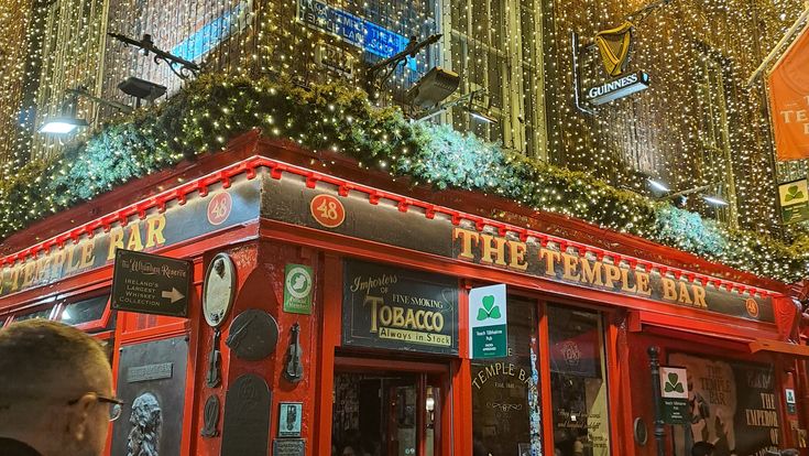 Die rot gestrichene Temple Bar in Dublin bei Nacht, umgeben von festlicher Beleuchtung und zahlreichen Gästen.
