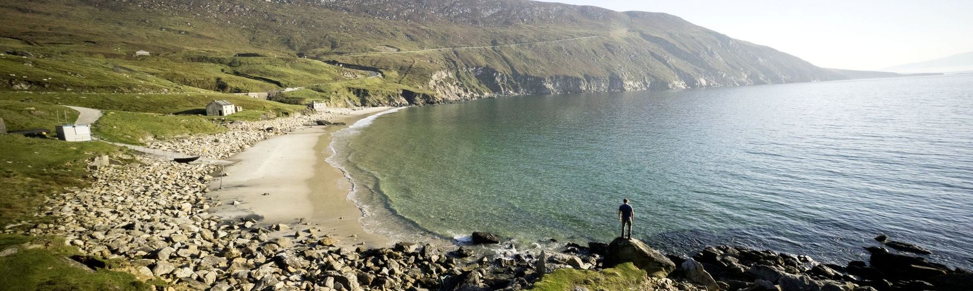 Ruhige Bucht mit steinigem Strand und grünen Hügeln an der wilden Küste Irlands.