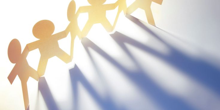 Papierfiguren, die sich an den Händen halten – Symbol für Teamarbeit, Zusammenhalt und Kooperation.