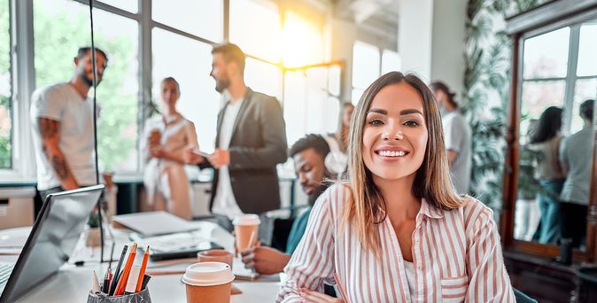 Lachende Frau im alternativen Büro mit Kaffeebecher und Kollegen