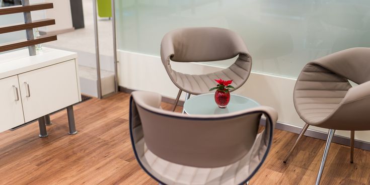 Moderner Wartebereich mit Designstühlen und kleinem Glastisch, auf dem eine rote Vase mit Blume steht – einladende Atmosphäre in einem Reisebüro.