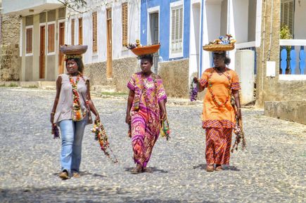 Frauen mit bunter Kleidung und Schalen auf dem Kopf spazieren die Straße hinab