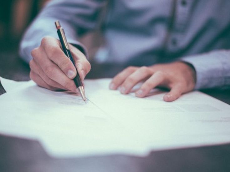 Person unterschreibt ein Dokument – Symbol für Vertrag, Vereinbarung oder Buchungsabschluss.