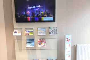 Wartebereich im Reisebüro mit Prospektwand, Bildschirm mit Shanghai-Motiv und Sitzgelegenheit für Kunden.