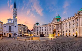 Der Michaelerplatz in Wien mit der barocken Hofburg und der St.-Michael-Kirche im Licht der Abenddämmerung.
