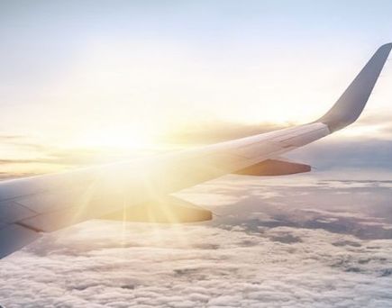 Flugzeugflügel über einer Wolkendecke bei Sonnenaufgang – Blick aus dem Fenster während des Flugs.