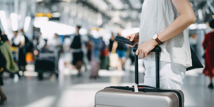 Frau mit Reisepass und Koffer in der Flughafenhalle