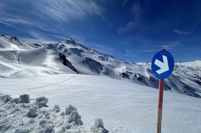 Schneebedeckte Skipiste mit blauen Markierungen und atemberaubendem Alpenpanorama.