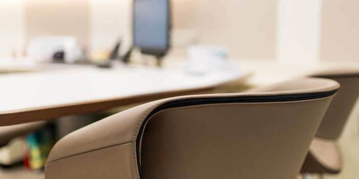 Detailaufnahme eines modernen Beratungsstuhls an einem Schreibtisch mit Computer im unscharfen Hintergrund.