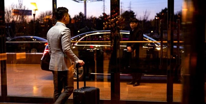 Chauffeurservice - Reisender mit Koffer geht am Flughafen durch eine Tür