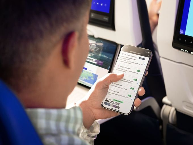 Mann an Bord von United Airlines mit Smartphone in der Hand und das Display zeigt die App / Wifi