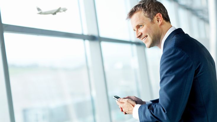 Mann mit Handy vor Flughafen-Fensterfront, Flugzeug im Hintergrund