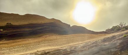 Karge, geschichtete Vulkanlandschaft im Teide-Nationalpark mit tief stehender Sonne und vereinzelten grünen Pflanzen.