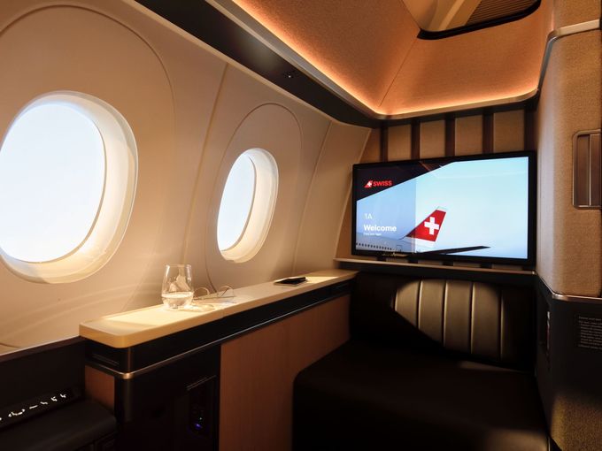 First Class Suite mit zwei Fenstern, Willkommensbildschirm für Sitz 1A und schwarzem Ledersitz.