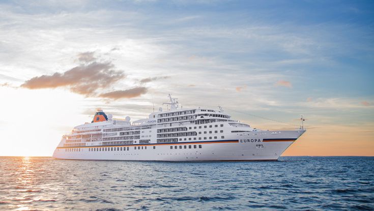 Kreuzfahrtschiff auf dem offenen Meer bei Sonnenuntergang, das im goldenen Licht des Himmels glänzt – Sinnbild für exklusive Reisen und Entspannung auf See.