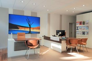 Beratungsplatz im Reisebüro mit großem Bildschirm, der eine Wüstenlandschaft zeigt, und moderner Einrichtung in warmen Farbtönen.