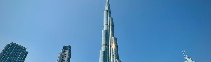 Burj Khalifa in Dubai umgeben von modernen Hochhäusern und Wasserbecken unter klarem, blauem Himmel.