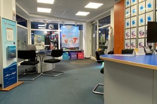 Innenansicht eines Reisebüros mit Schreibtisch, Prospektwand und Schaufenster im Hintergrund.