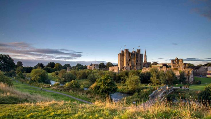Alte Burg inmitten weiter Landschaft mit grünen Wiesen und bewölktem Himmel.