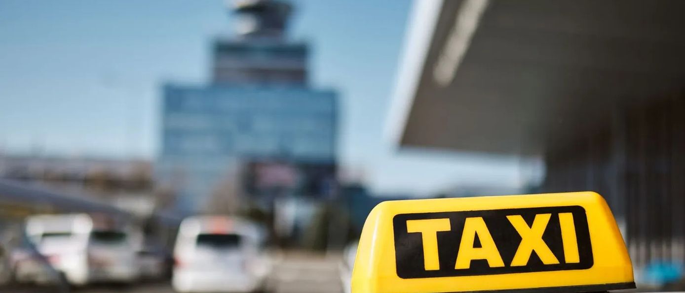 Gelbes Taxischild auf einem Taxi vor einem Flughafen, Taxikosten-Ranking in Deutschland für Geschäftsreisende