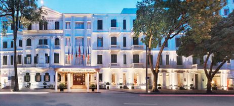 Weißes Hotel mit Bäumen im Vordergrund und leichter Beleuchtung 