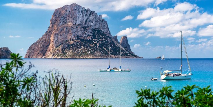 Blick auf die markante Felseninsel Es Vedrà vor der Küste Ibizas mit Segelbooten im türkisblauen Mittelmeer.