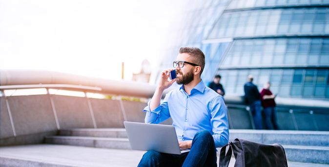 Geschäftsmann auf Brücke sitzend mit Handy, Laptop und Tasche