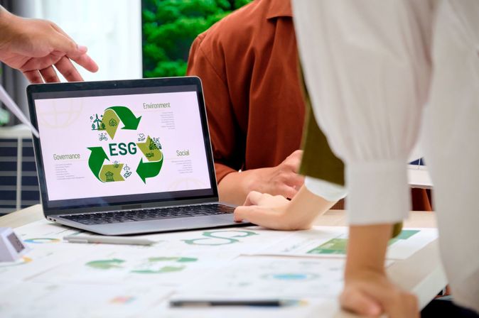 Laptop zeigt ESG-Grafik (Environment, Social, Governance) während eines Meetings mit mehreren Personen am Tisch.