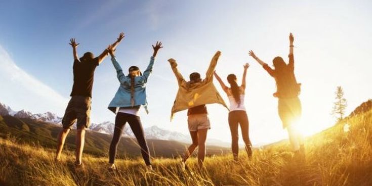 Gruppe junger Menschen mit erhobenen Armen im Sonnenlicht einer Berglandschaft – Symbol für Freundschaft, Abenteuer und Lebensfreude.