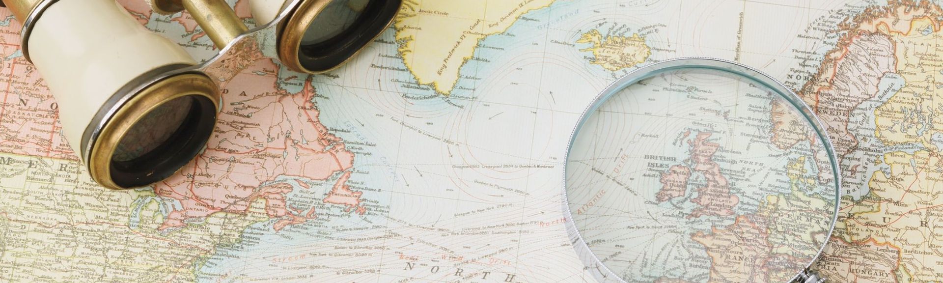 Alte Weltkarte mit einem Fernglas, einer Lupe und einigen Münzen – Symbol für Reiseplanung, Entdeckung und Fernweh.