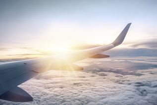Blick aus dem Flugzeugfenster auf den Flügel über einer Wolkendecke bei Sonnenaufgang.
