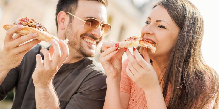 Lachendes Paar isst gemeinsam Pizza im Freien – Symbol für Genuss, Lebensfreude und gemeinsame Auszeit auf Reisen.