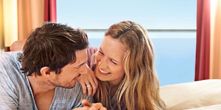 Paar liegt auf dem Bett mit Blick durch die offene Balkontür auf das Meer