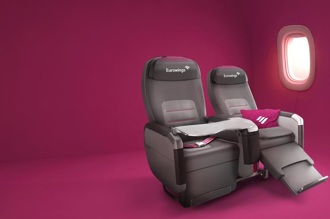 Eurowings-BIZclass-Sitz in Liegeposition mit Kissen und Decke vor pinkfarbenem Hintergrund