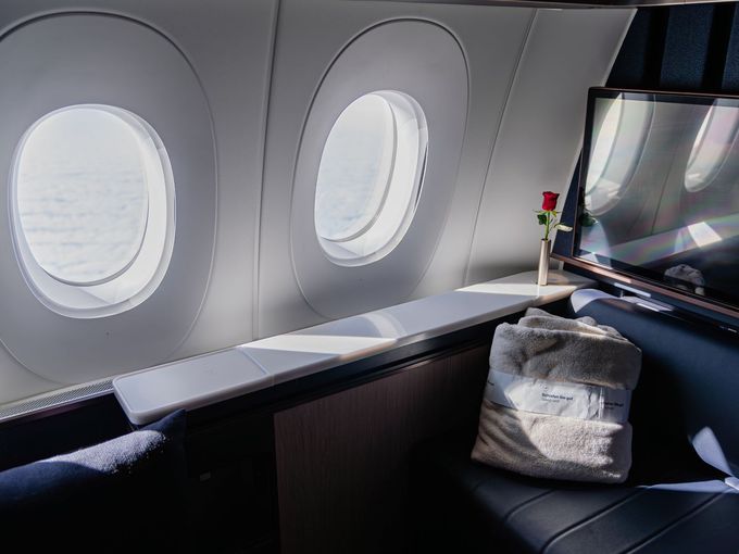 Lufthansa First-Class-Sitz mit zwei Fensterluken, roter Rose auf der Ablage, gefaltetem Handtuch und Bildschirm.