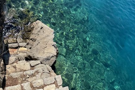 Steintreppe führt ins klare, türkisfarbene Wasser mit sichtbarem felsigen Grund.