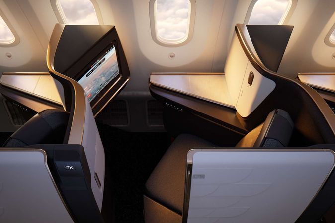 Moderne Business Class Sitze im Flugzeug mit großem Touchscreen-Monitor, in elegantem Gold-Weiß-Design mit Blick auf die Kabinenfenster.