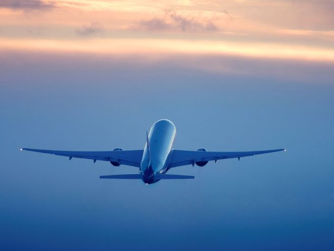 Passagierflugzeug im Steigflug vor farbigem Abendhimmel.