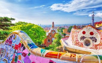 Farbmosaike und Aussicht auf die Stadt Barcelona im Park Güell mit Blick bis zum Meer an einem sonnigen Tag.