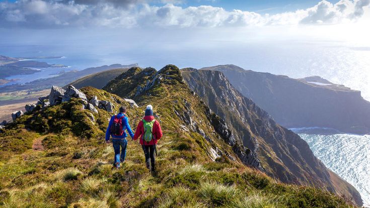 Zwei Wanderer laufen über einen schmalen Berggrat mit spektakulärem Blick auf die Küste und das Meer in Irland.