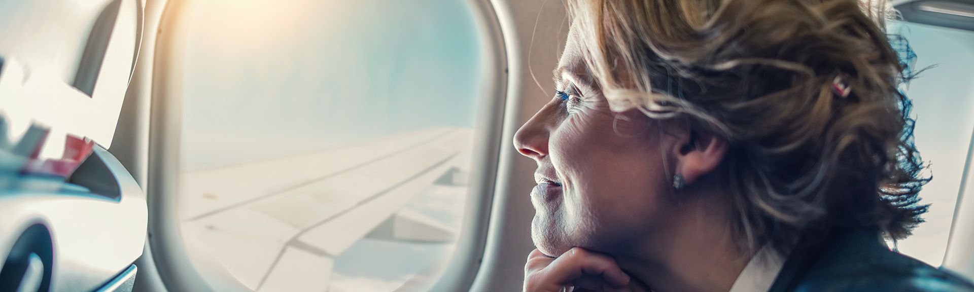 Frau sieht lächelnd aus dem Fenster eines Flugzeugs
