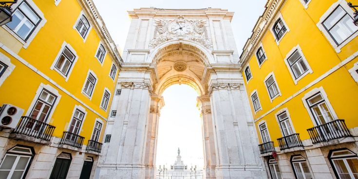 Blick auf den monumentalen Triumphbogen Arco da Rua Augusta zwischen gelben Gebäudefassaden in Lissabon.