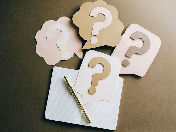 Notizbuch mit goldenem Stift und mehreren Sprechblasen mit Fragezeichen – Symbol für Fragen, Ideen oder häufig gestellte Fragen (FAQ)