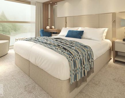 Eine helle und einladende Schiffskabine mit einem komfortablen Bett, eingebauten Schränken, einer kleinen Sitzecke und einem großen Flachbildfernseher.